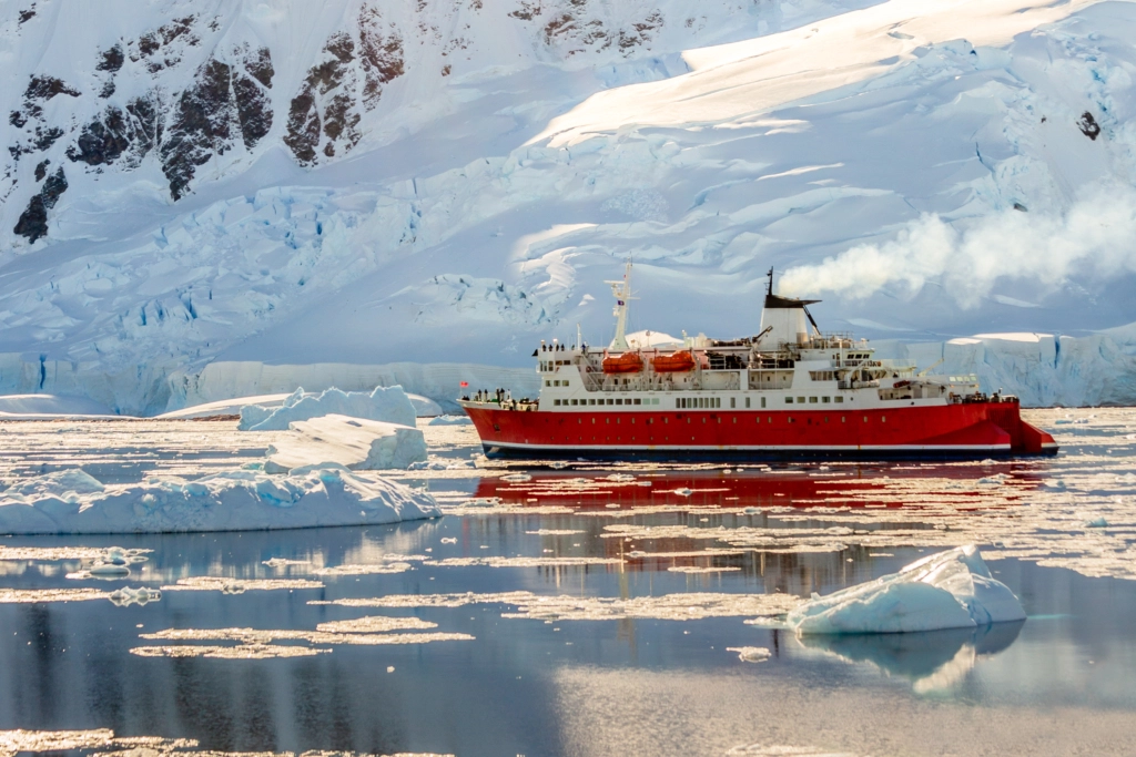 Red cruise steamboat drifting among the icebergs with huge rock